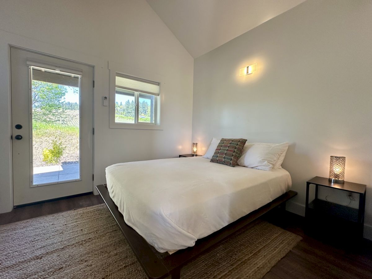 A minimalist bedroom with a bed, two side tables with lamps, a rug, and a door with a window view.