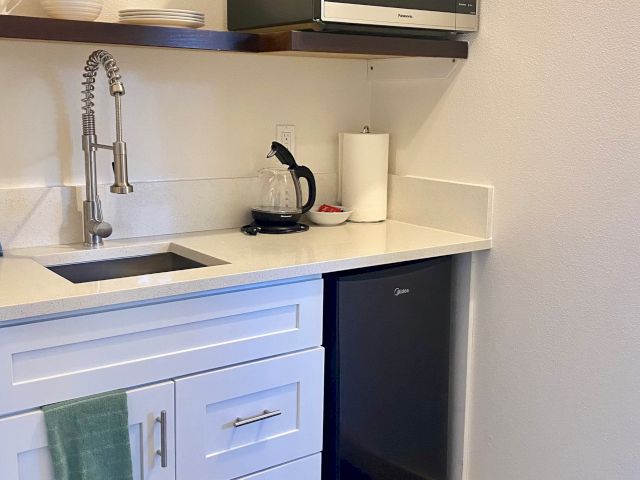 A small kitchenette with a sink, faucet, mini-fridge, microwave, and countertop with a coffee maker and paper towel holder.