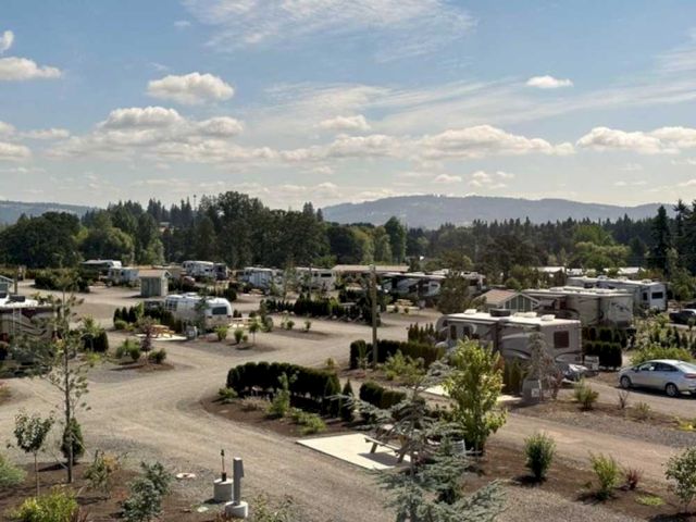 A scenic RV park with various parked RVs, surrounded by greenery and trees under a partly cloudy sky, with distant hills.