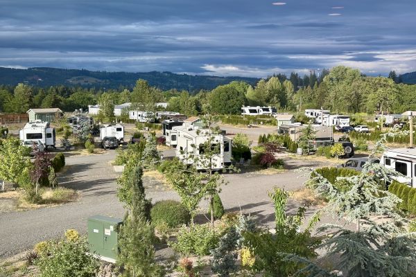 A scenic RV park with numerous trailers, greenery, and distant hills under a cloudy sky.