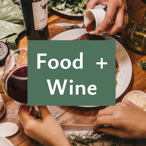 A group dining scene with someone pouring red wine beside plates, showing a &ldquo;Food + Wine&rdquo; theme.